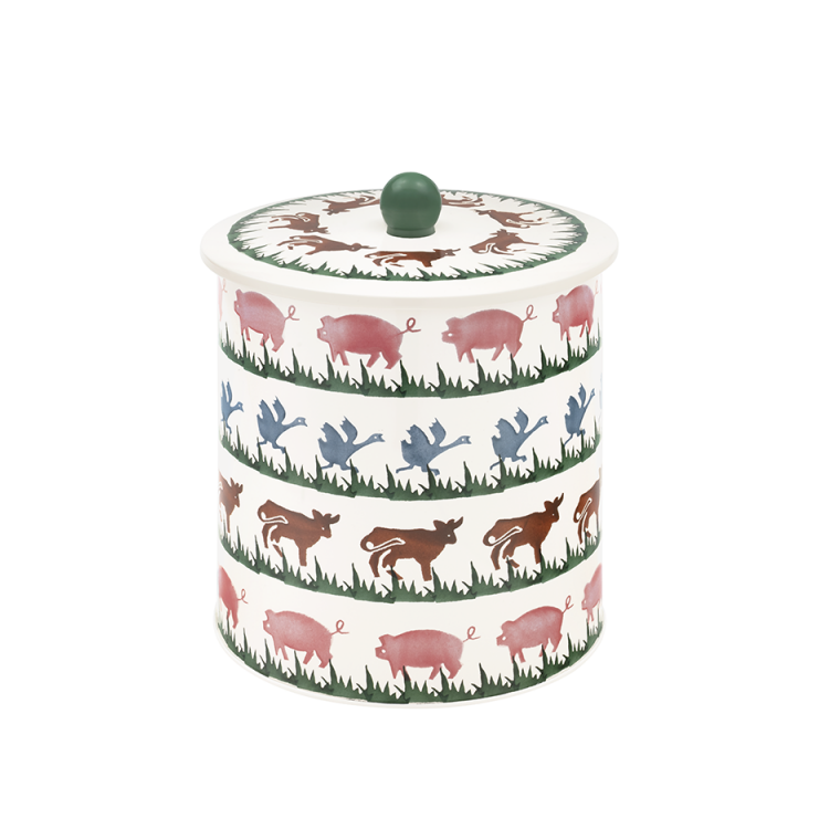 A cylindrical lidded ceramic container with a white background and a repeating pattern of pink pigs, green grass, and blue and brown birds, topped with a small green knob.