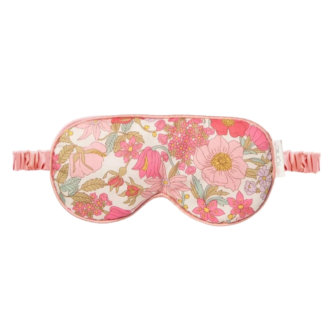 A floral sleep mask with a pink and cream pattern, featuring a matching pink elastic strap, shown against a plain white background.