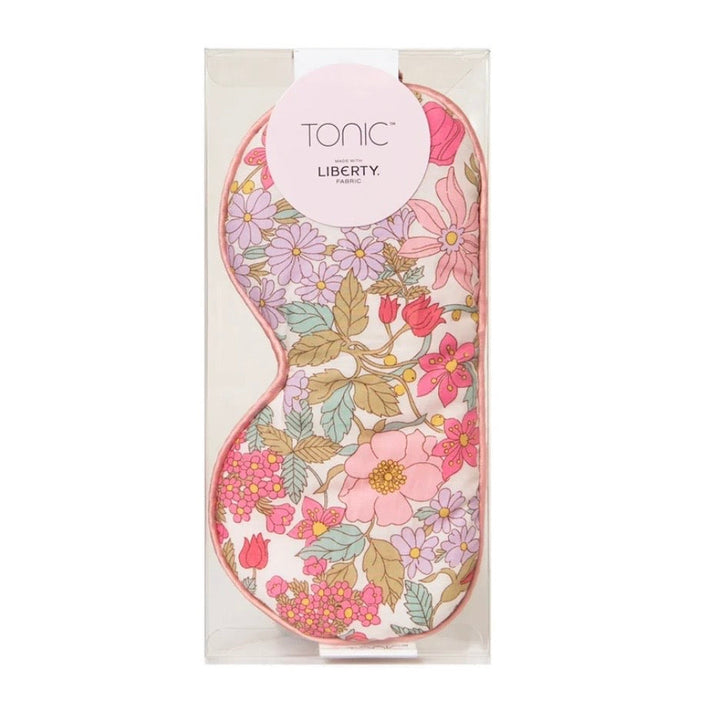 A floral-patterned sleep mask in its clear plastic packaging, featuring a pink and multicolor botanical print with a circular pink &