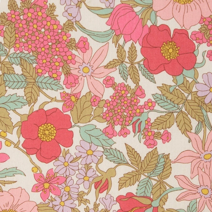 A close-up of a floral fabric pattern featuring large pink and red flowers, smaller lavender blossoms, and green and tan leaves on a warm cream background.