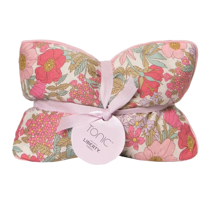 A folded fabric product with a pink floral print, tied with a light pink ribbon and a round paper tag that reads &