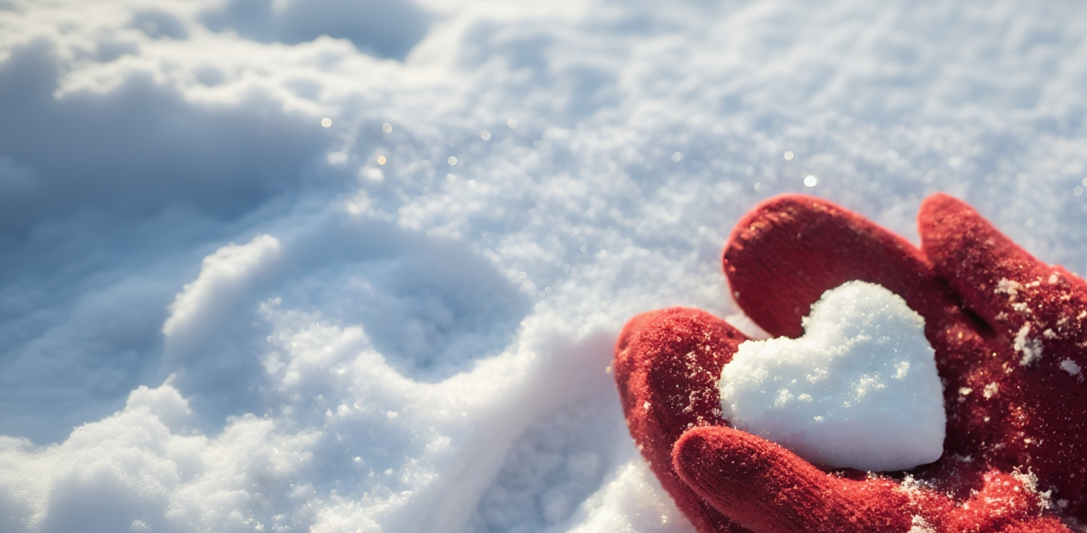 Red gloves holding a heart-shaped snowball on a snowy background
