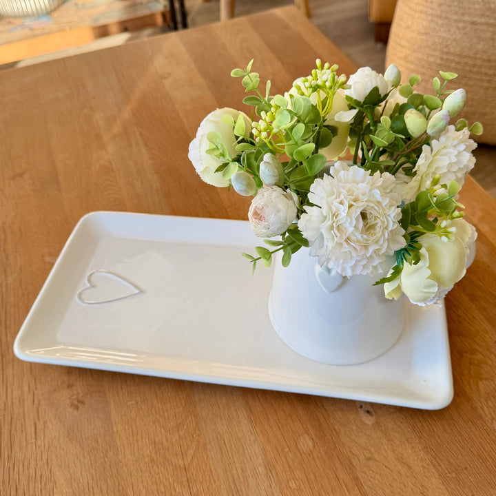 White vase with flowers on a white tray on a wooden table