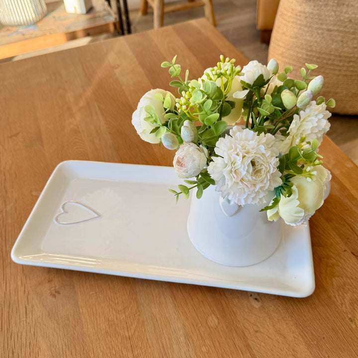 White vase with flowers on a white tray on a wooden table
