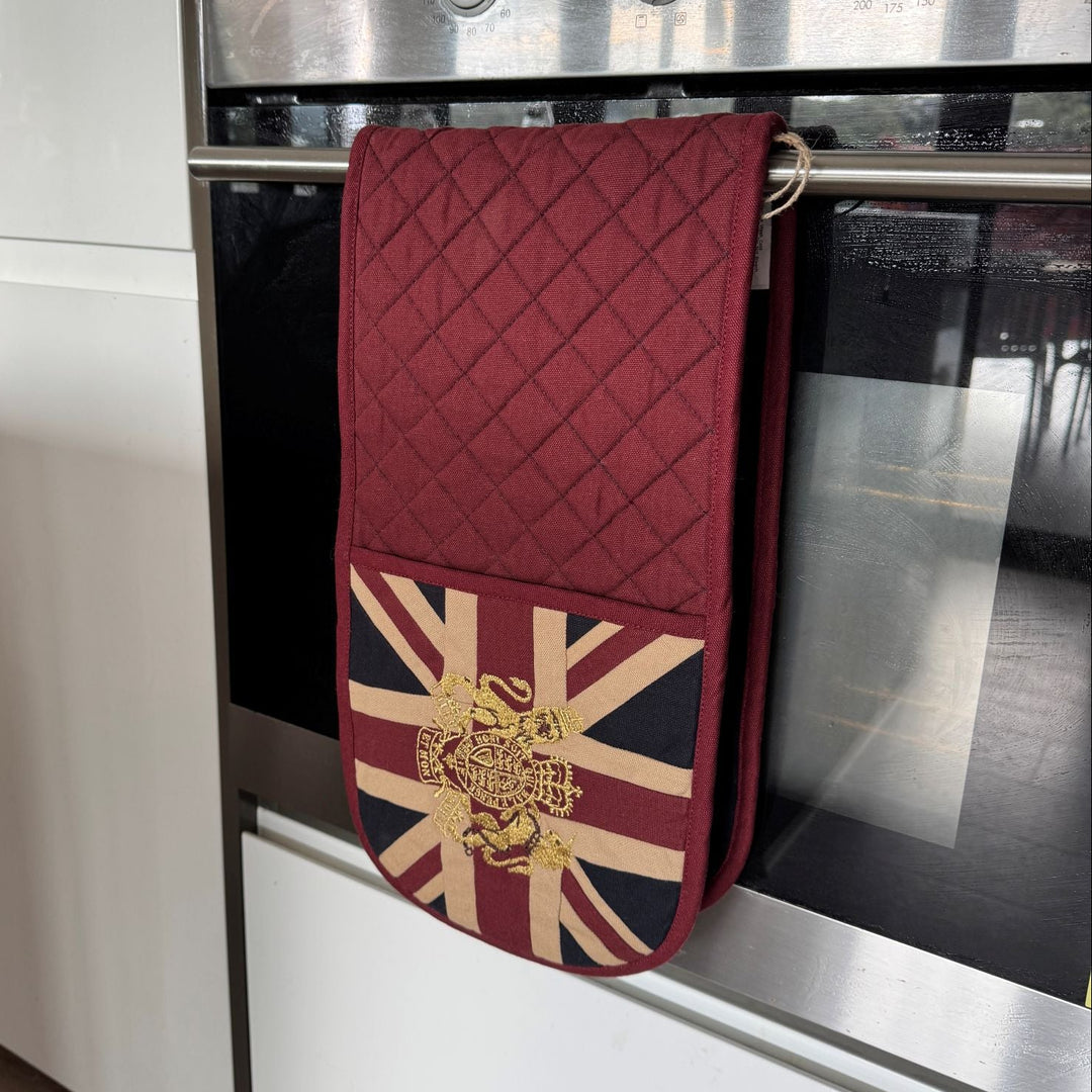 Red quilted oven mitt with Union Jack design hanging on a silver oven door.