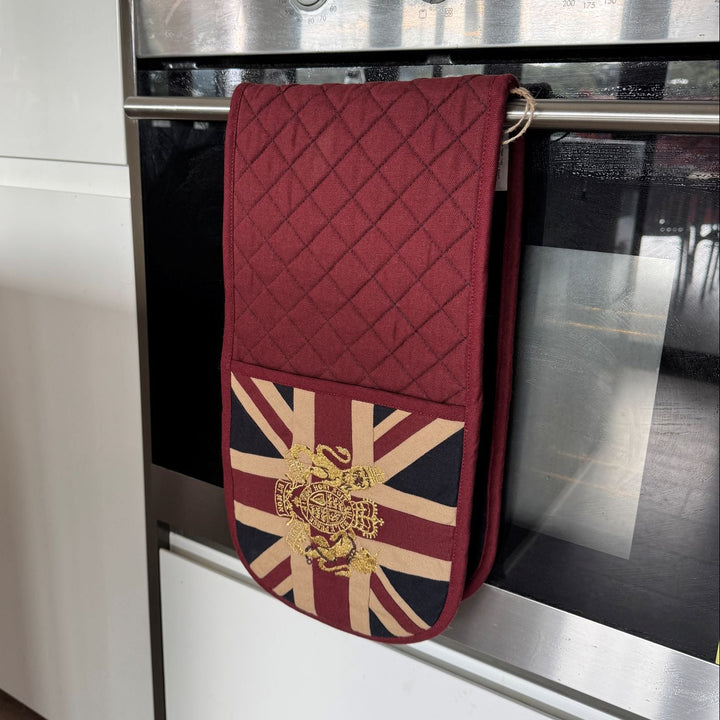 Red quilted oven mitt with Union Jack design hanging on a silver oven door.